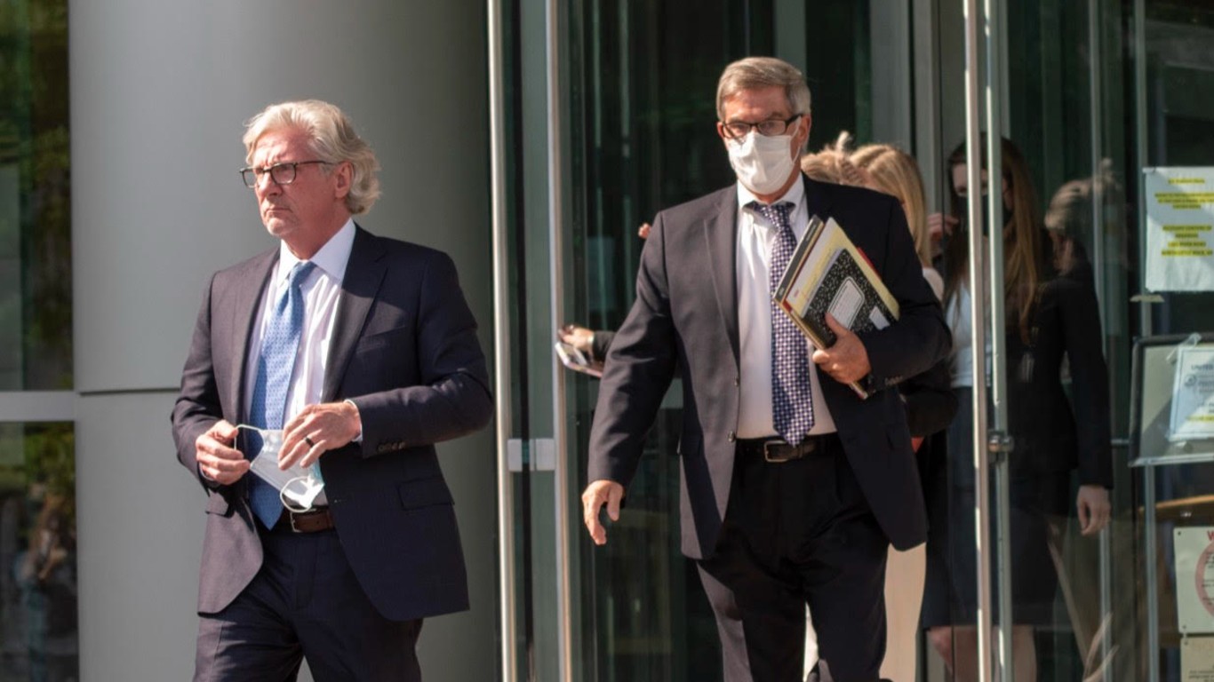 The defendant leaves the courthouse wearing a mask and carrying papers. He's wearing a suit and tie.