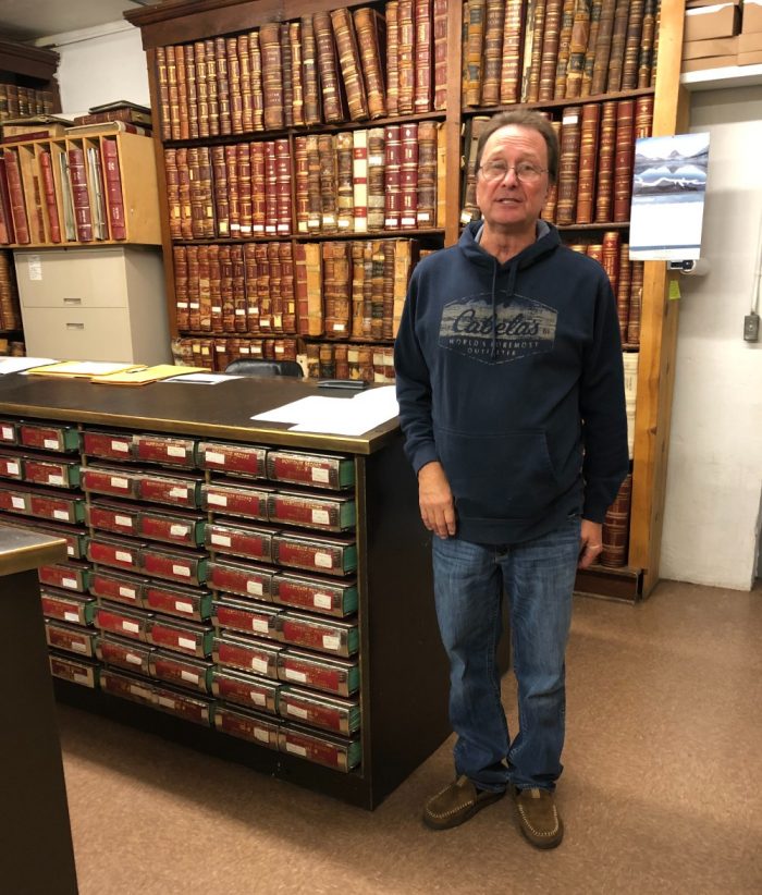A man in a sweatshirt surrounded by giant old books of property records